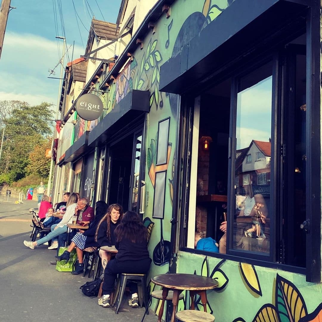 Visitors enjoying outdoor seating at Number 8, a café with vibrant green floral mural on the exterior, on a sunny day.