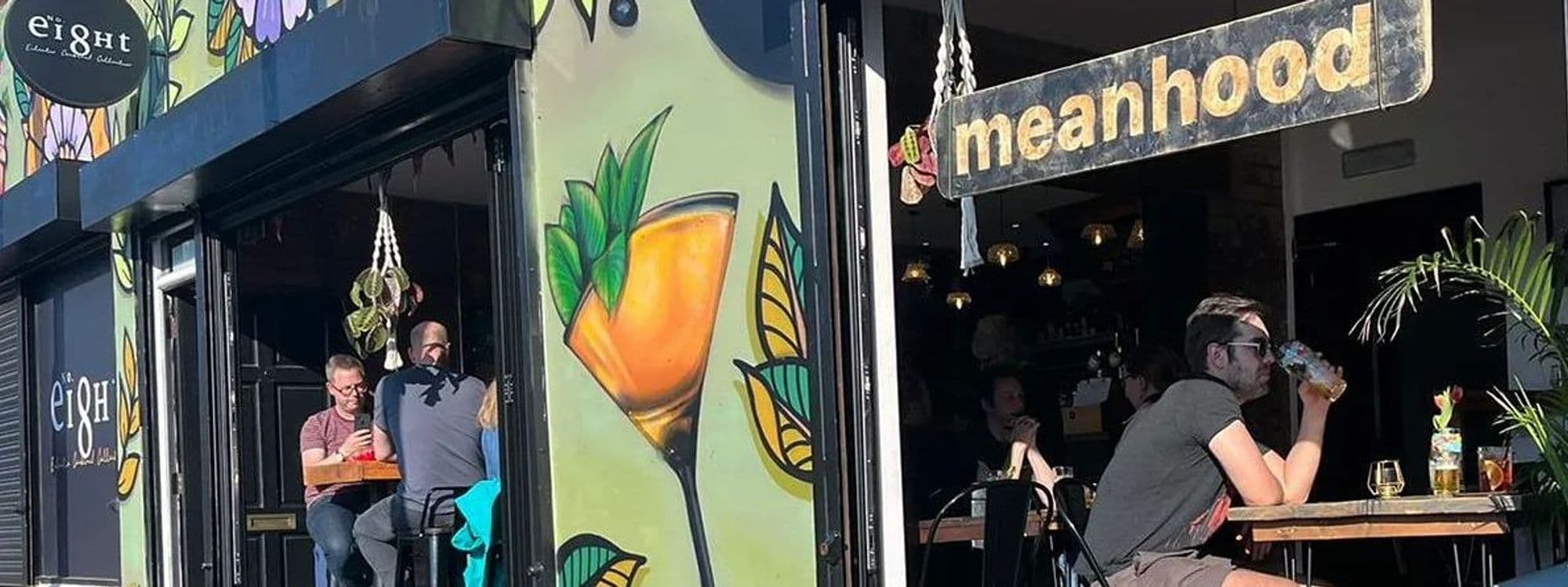 Patrons enjoying drinks on a sunny day at Number 8 bar with vibrant mural artwork and cozy outdoor seating.