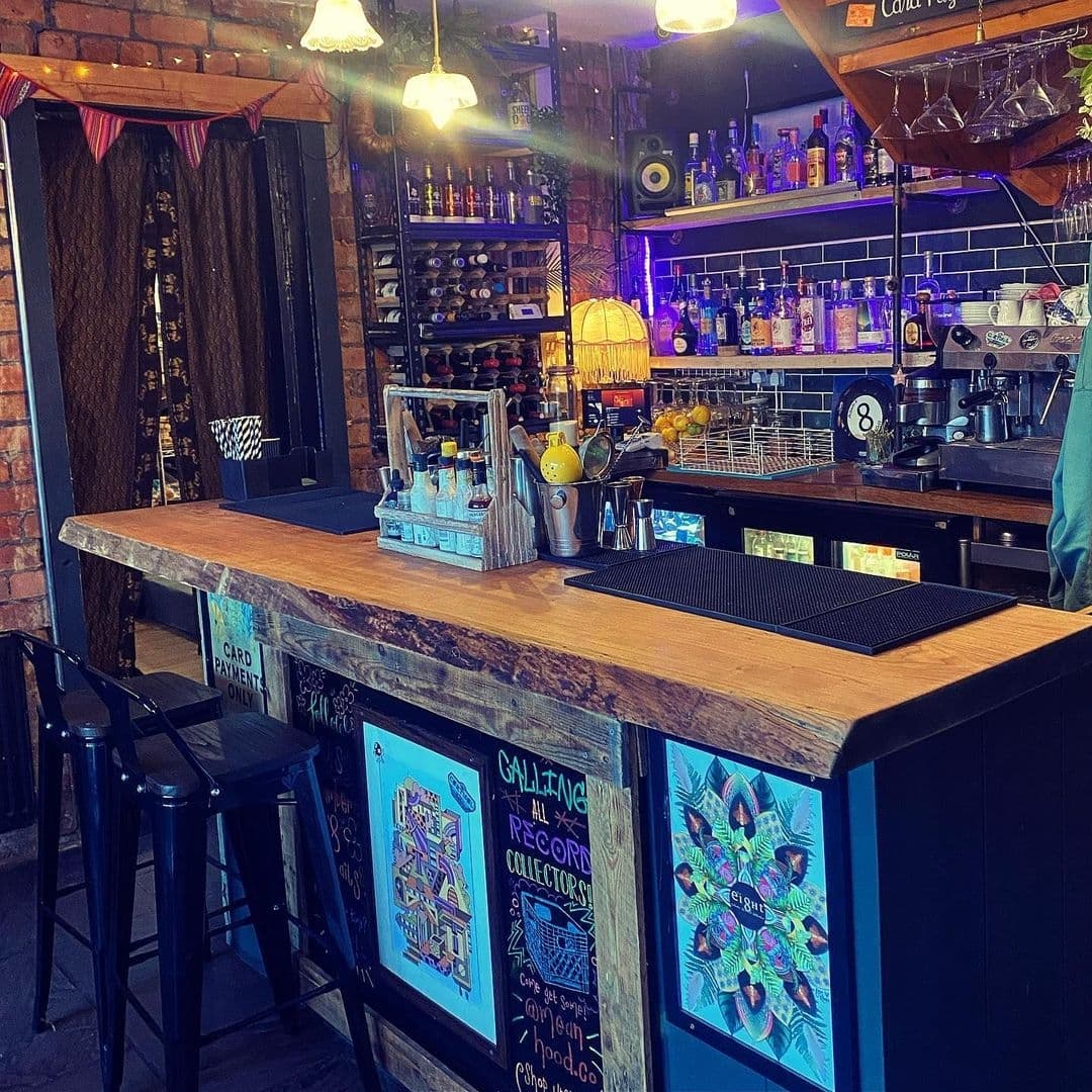 Interior of Number 8 featuring a cozy bar area with exposed brick walls, hanging lights, and a variety of spirits on shelves. A barista station and colorful chalkboard menus add to the inviting atmosphere.