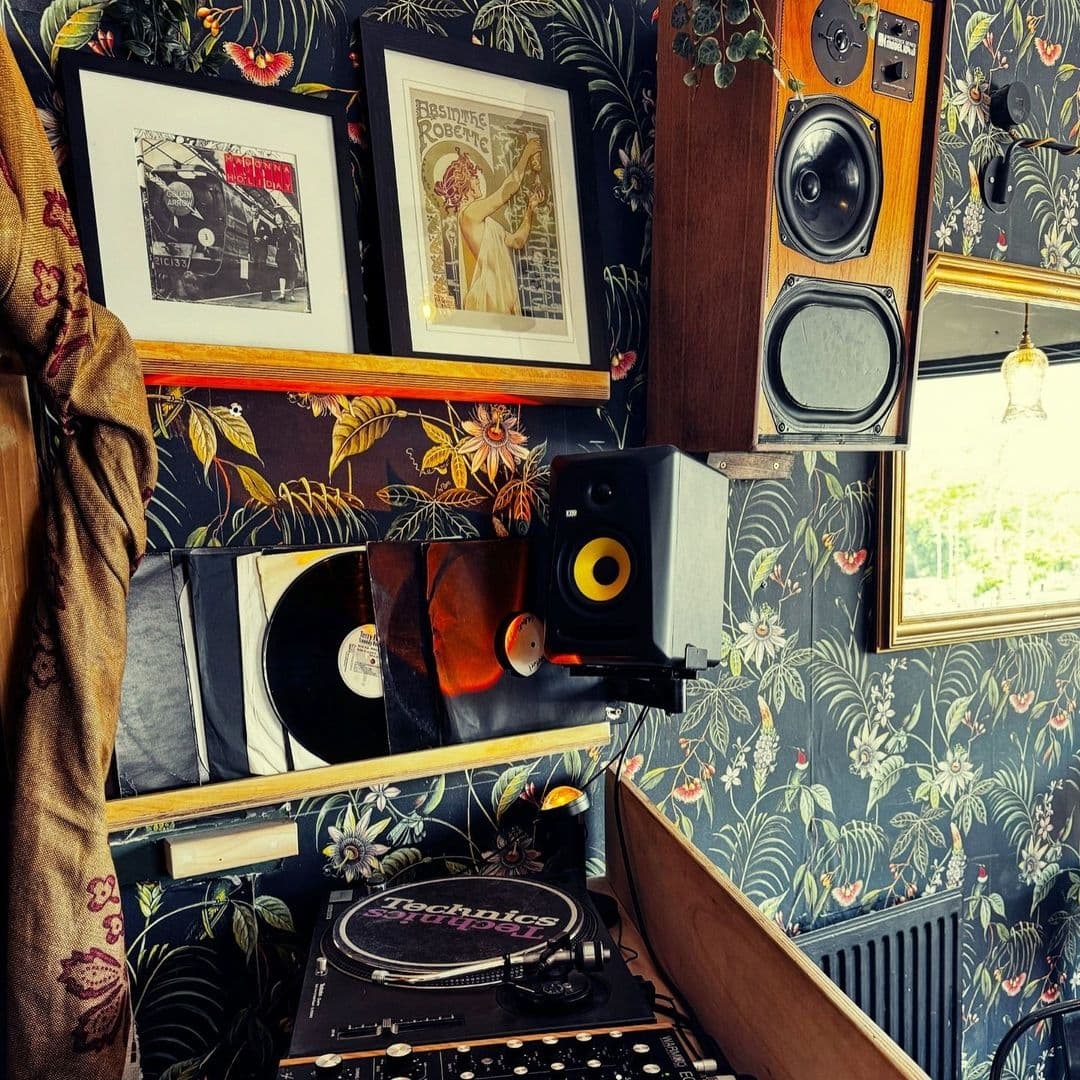 Interior corner of Number 8 featuring a vintage-style setup with a turntable, vinyl records, framed artwork, and speakers against a floral wallpaper background.