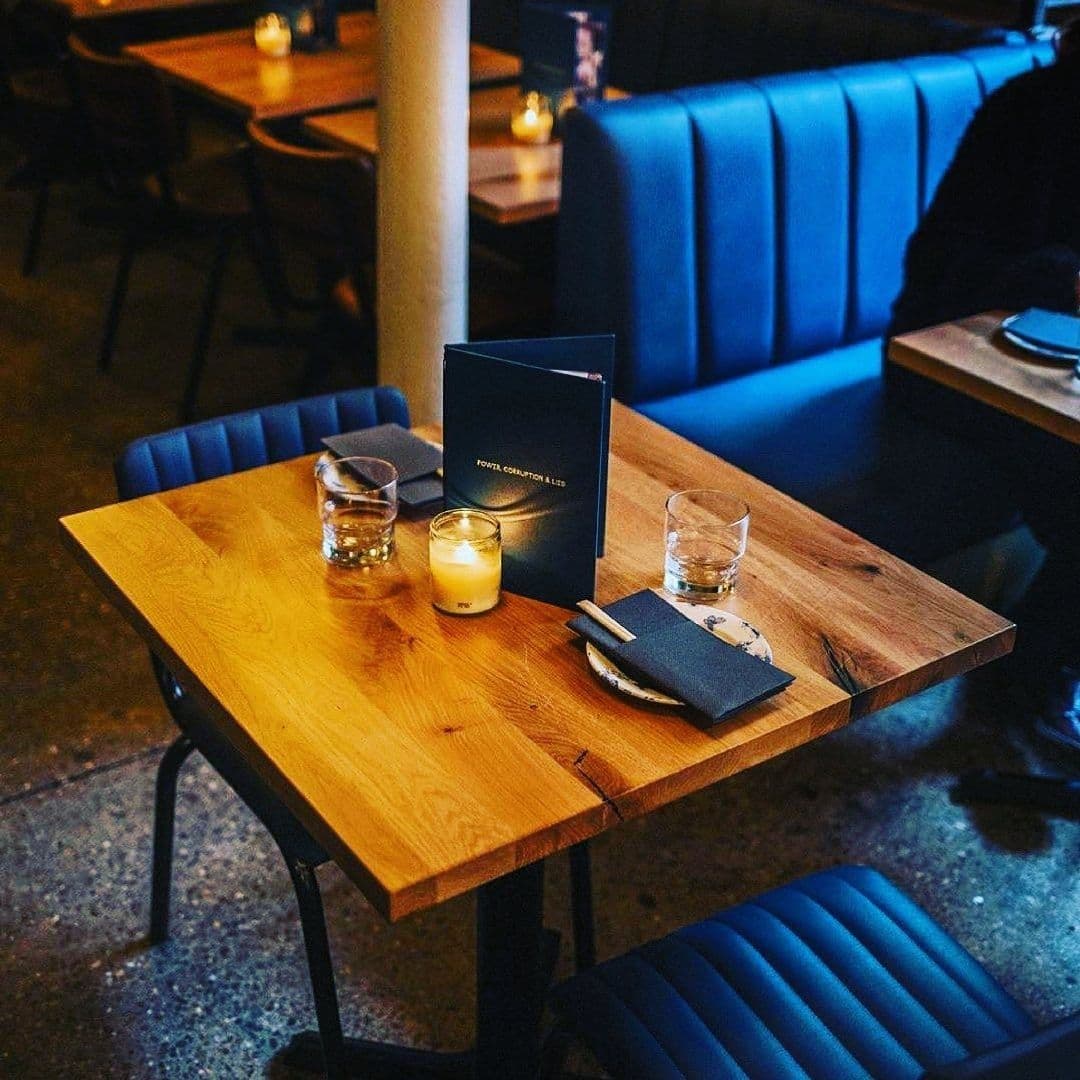 Intimate dining setting at Power, Corruption & Lies with a wooden table, lit candles, and a menu on the table, surrounded by blue upholstered seating.