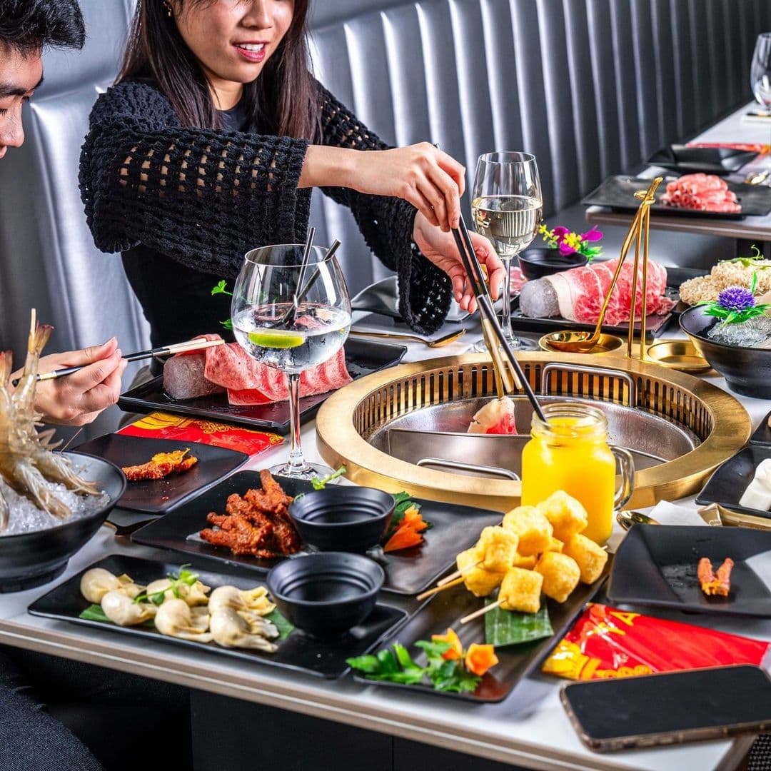 Diners enjoying a gourmet meal with a variety of meats and vegetables at TAO's interactive cooking table, complete with a built-in grill and elegant table setting.