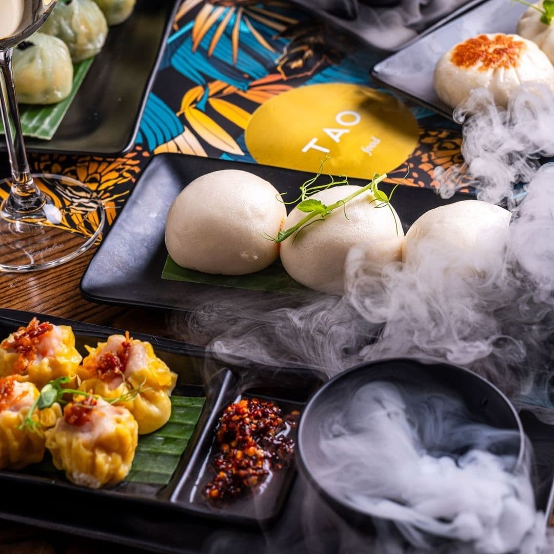 Gourmet Asian cuisine at TAO featuring steamed buns, dumplings, and a dramatic presentation with dry ice smoke.