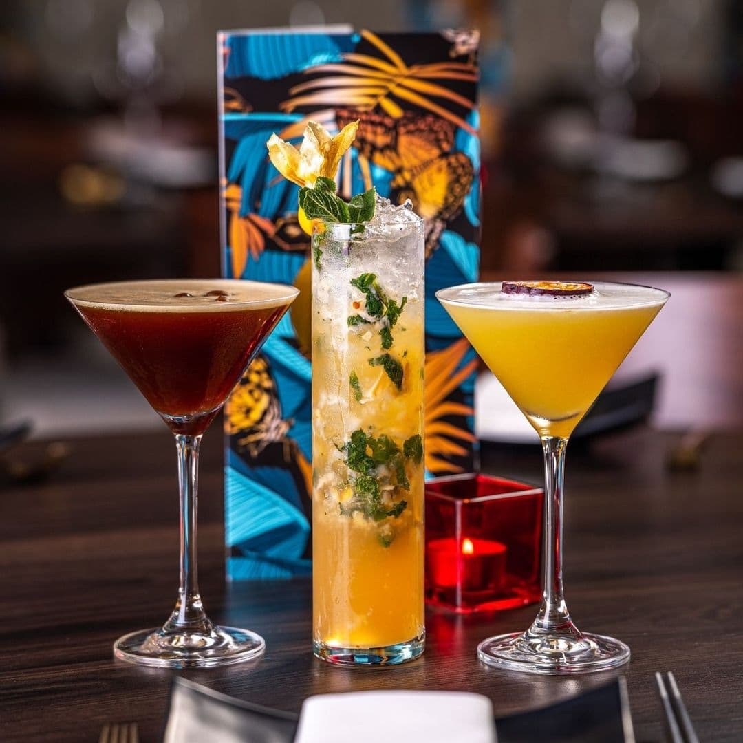 Alt text: "A variety of crafted cocktails on a table at TAO, featuring a dark espresso martini, a tall mojito with fresh mint, and a citrusy cocktail garnished with a dried orange slice."