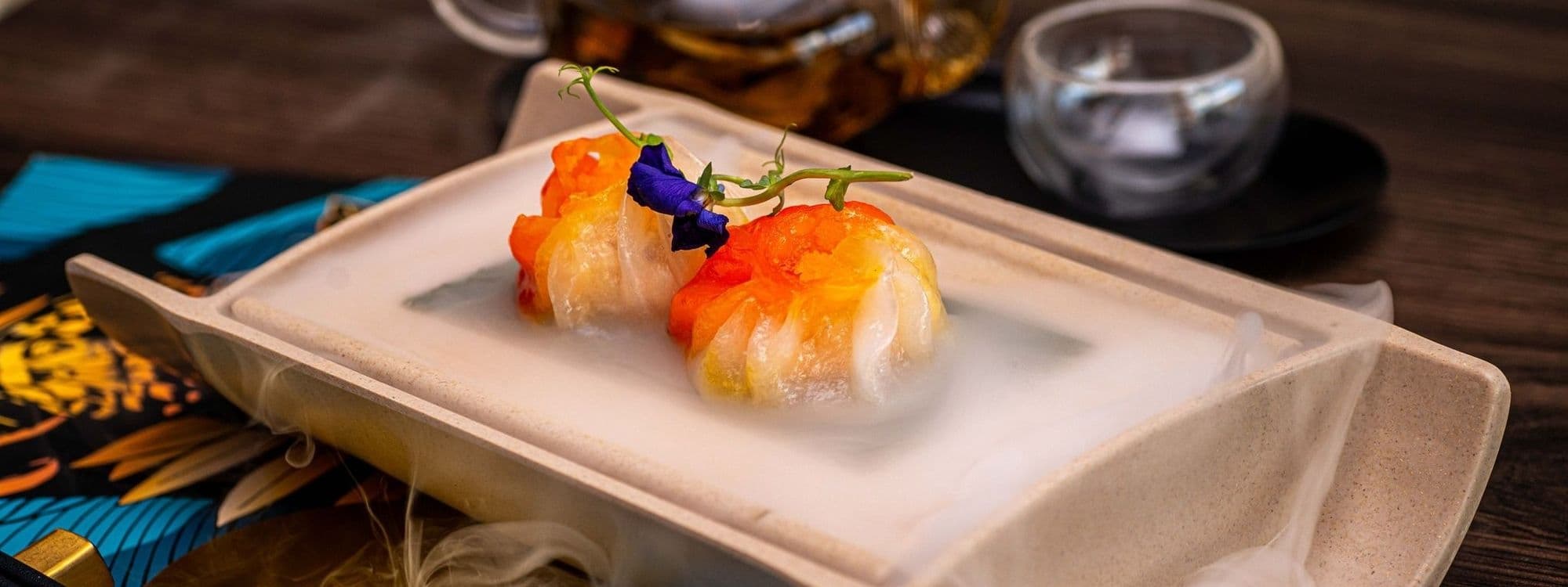 Gourmet sushi presentation at TAO with colorful rolls on a misty, white rectangular plate, accented with a vibrant blue edible flower.