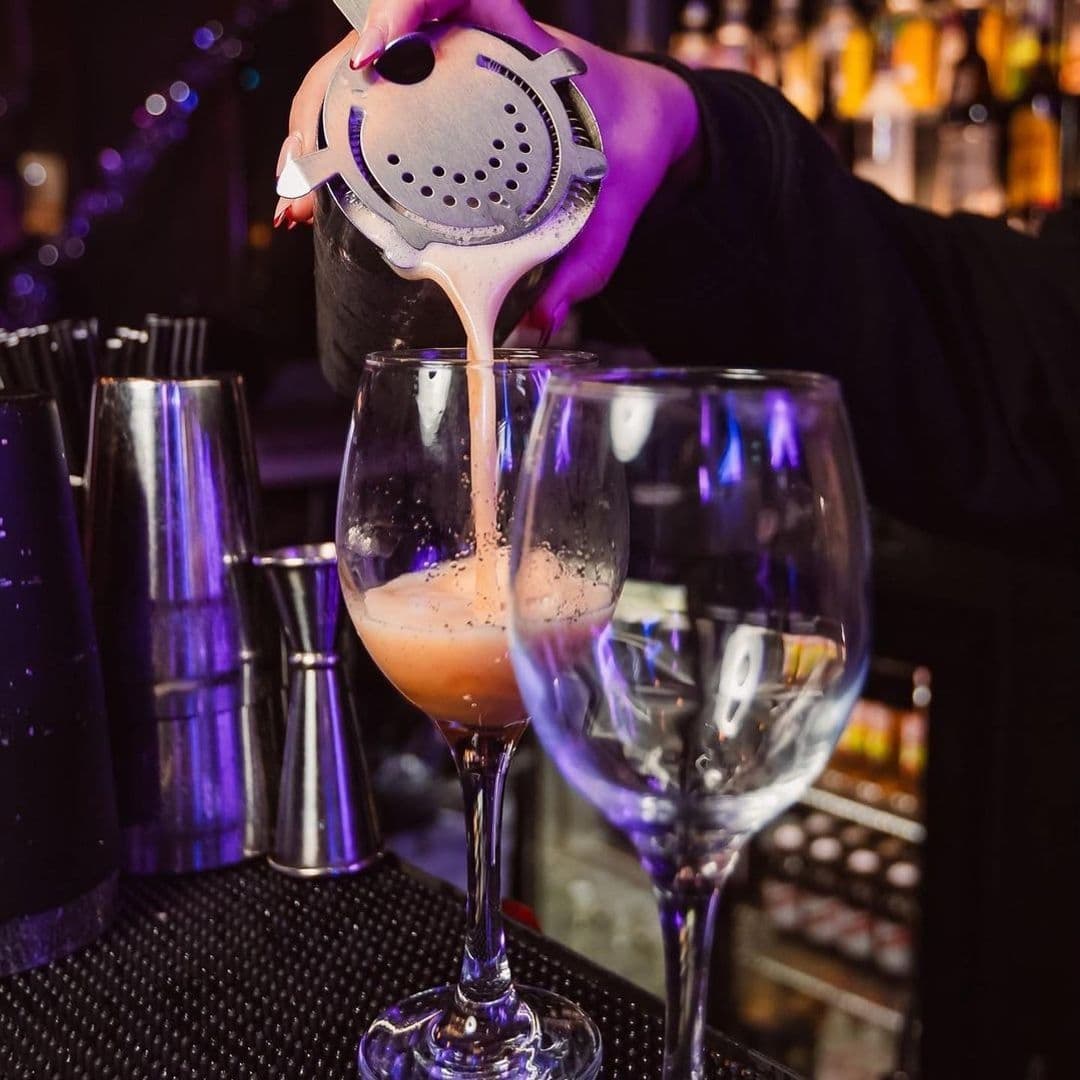 Bartender pouring a cocktail through a strainer into a glass at Ten Bar.