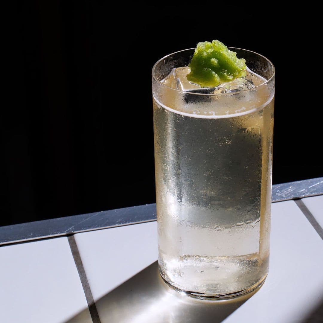 Chilled cocktail with lime garnish at Test Bar, served on a tiled table with a contrasting dark background.