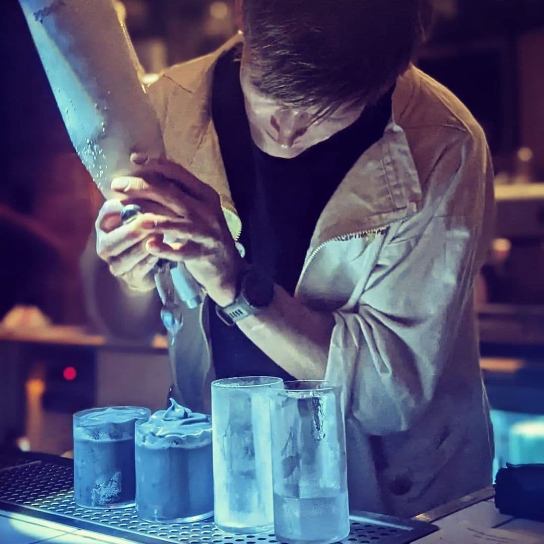 Bartender carefully chiseling a large block of ice to fit into glasses at Test Bar, showcasing the craft of cocktail preparation.
