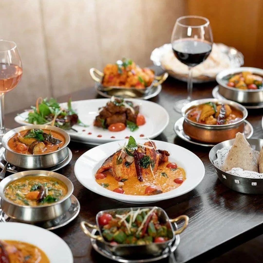 Assorted traditional Indian dishes served at Tharavadu, featuring curries, grilled fish, and bread, accompanied by glasses of red and rosé wine.