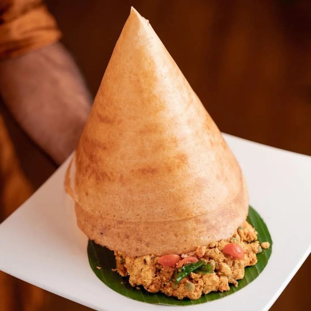 Crispy cone-shaped dosa on a banana leaf with savory filling at Tharavadu restaurant.