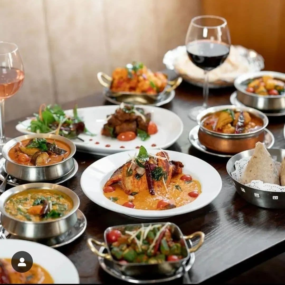 Assorted traditional Indian dishes and glasses of wine on a table at Tharavadu restaurant.