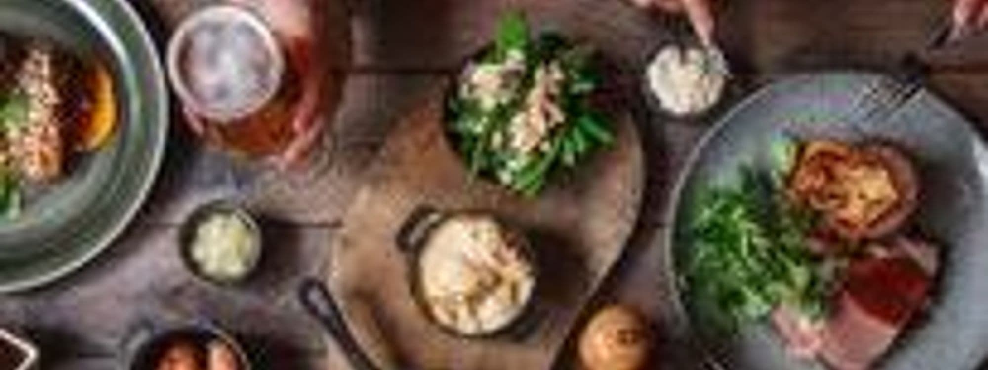 Gourmet dining experience at The Botanist Trinity featuring a variety of dishes and drinks on a rustic wooden table, including grilled meats, fresh greens, and craft beers.