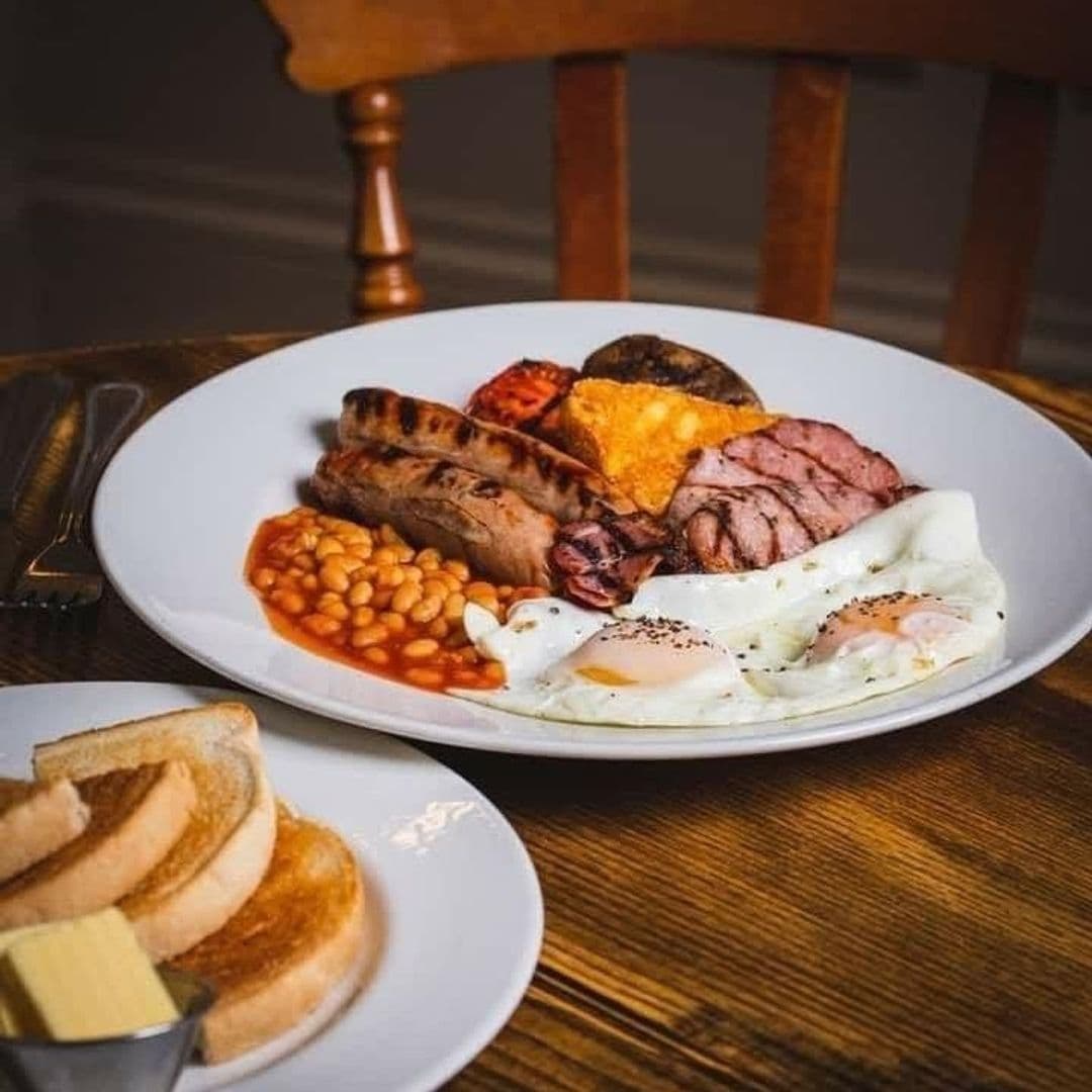 Traditional full English breakfast served at The Brown Cow, featuring eggs, sausage, bacon, black pudding, hash brown, grilled tomato, baked beans, and toast with butter on the side.
