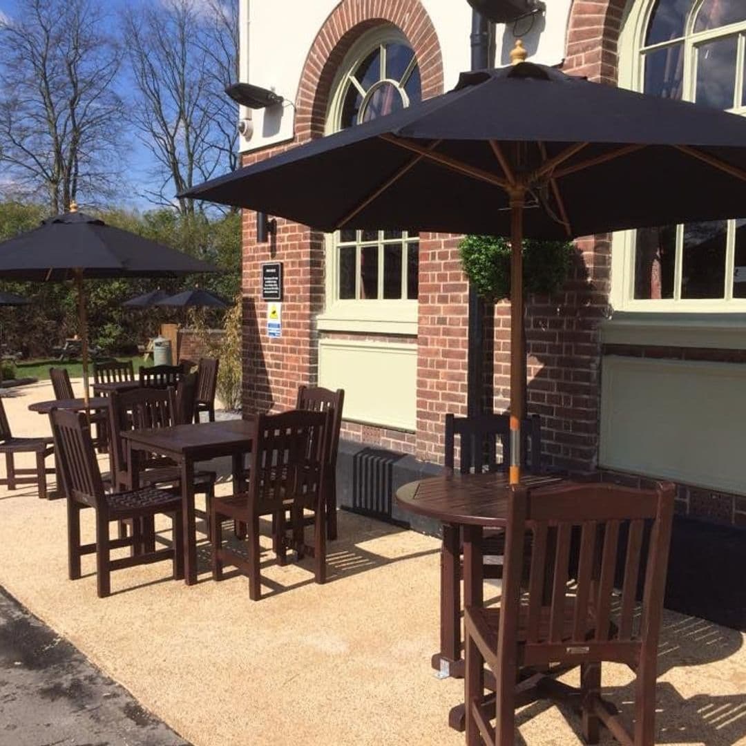 Outdoor seating area at The Brown Cow with wooden tables and chairs under sun umbrellas on a sunny day.