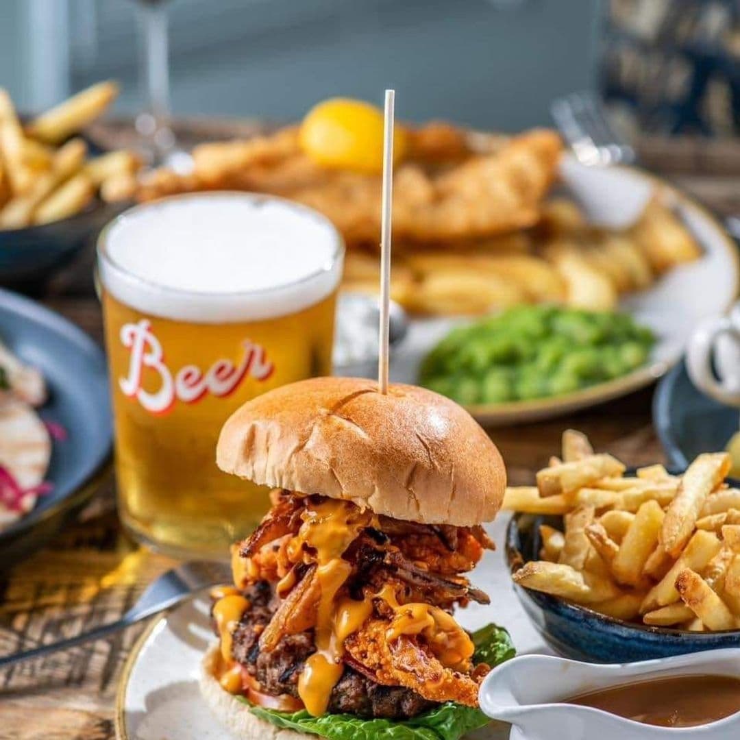 Alt text: "Savor the flavors at The Brown Cow with a mouth-watering stacked burger accompanied by a pint of beer, crispy fries, and traditional sides."