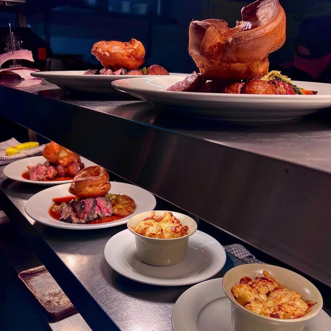 Traditional Sunday roast meals prepared at The Cross Keys, featuring Yorkshire puddings, roasted meats, and side dishes of vegetables on a kitchen counter ready to be served.