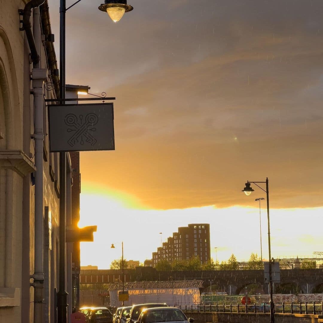 Sunset view at The Cross Keys with warm golden hues in the sky, street lights on, and a sign featuring crossed keys silhouetted against the evening glow.