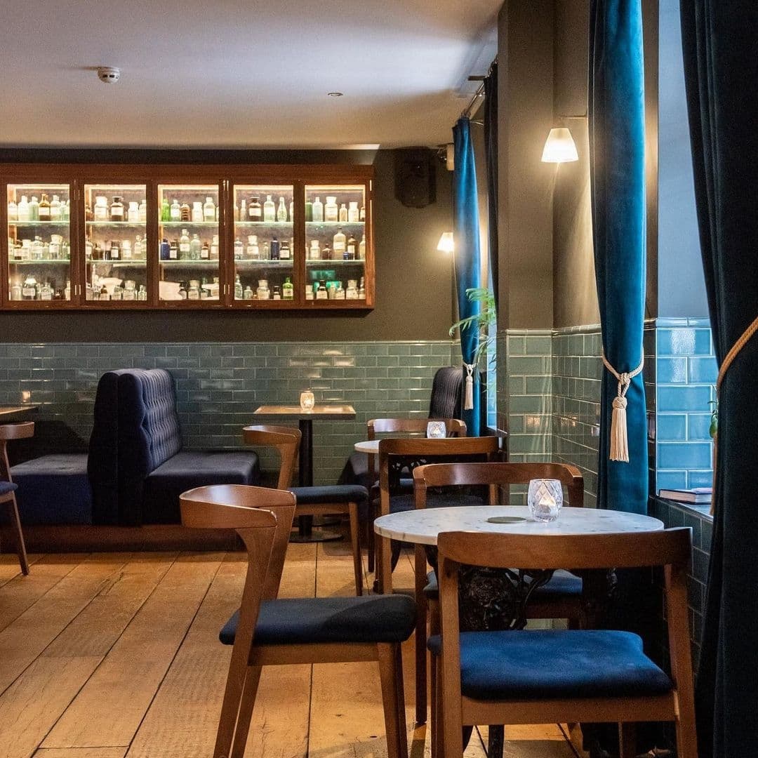 Interior of The Turk’s Head showcasing a cozy pub atmosphere with wooden tables, comfortable seating, blue drapery, and a well-stocked bar with various bottles in the background.
