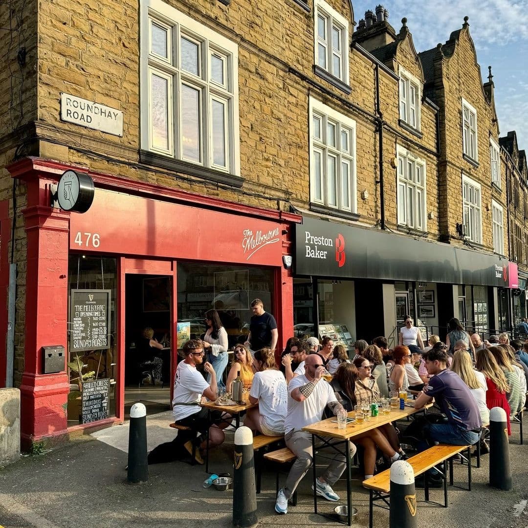 People enjoying outdoor seating at The Melbourne cafe on a sunny day, with a bustling atmosphere on Roundhay Road.