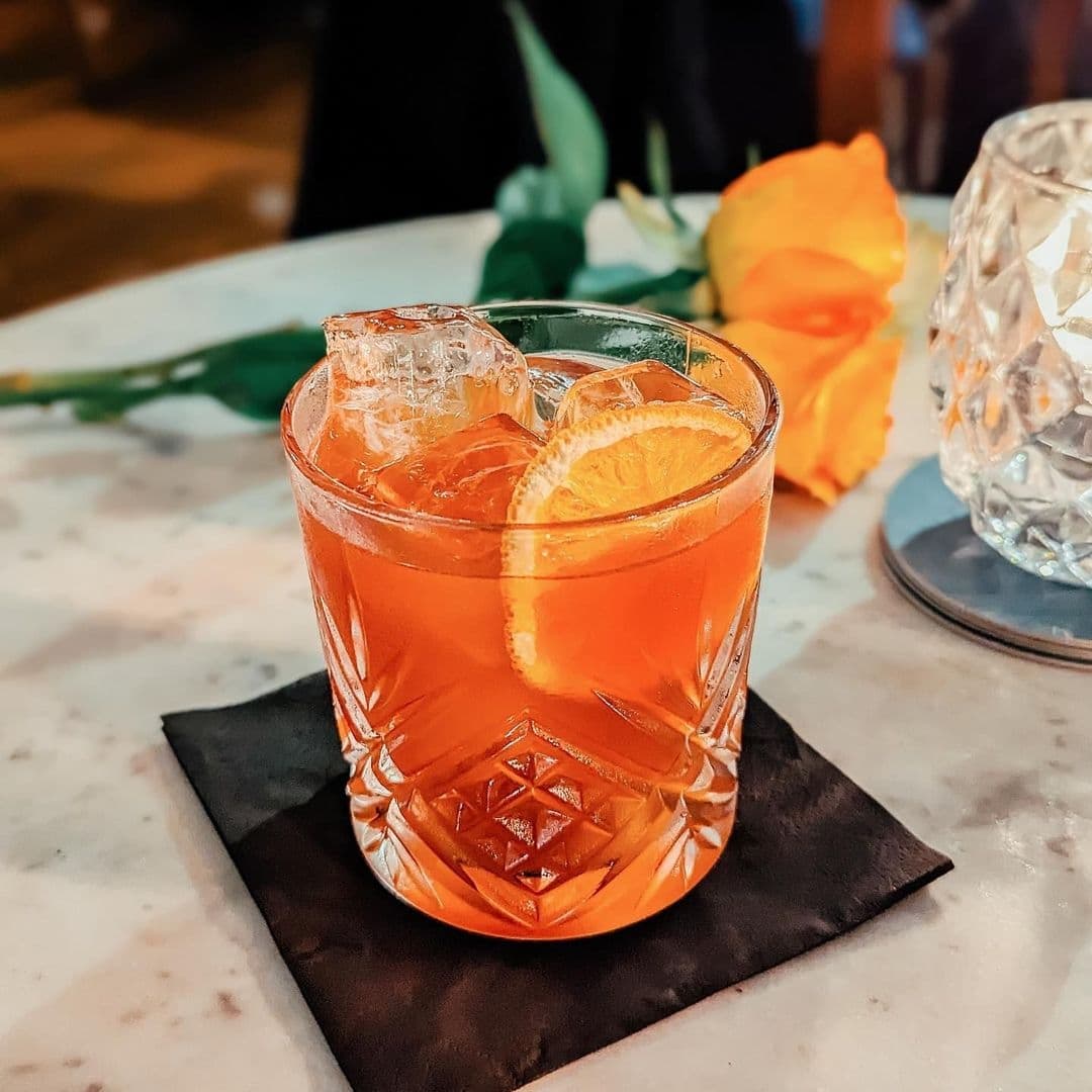 Orange cocktail with ice and a slice of orange, served on a black napkin at The Turk’s Head.