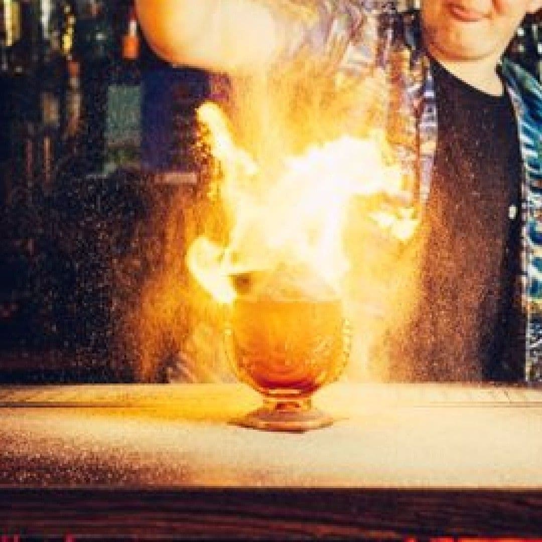 Flaming cocktail being prepared at Tiki Hideaway, with bartender in the background.