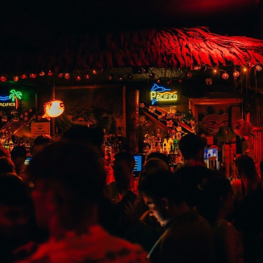 Vibrant atmosphere at Tiki Hideaway with patrons enjoying the dimly lit bar adorned with tropical decor and neon signs.