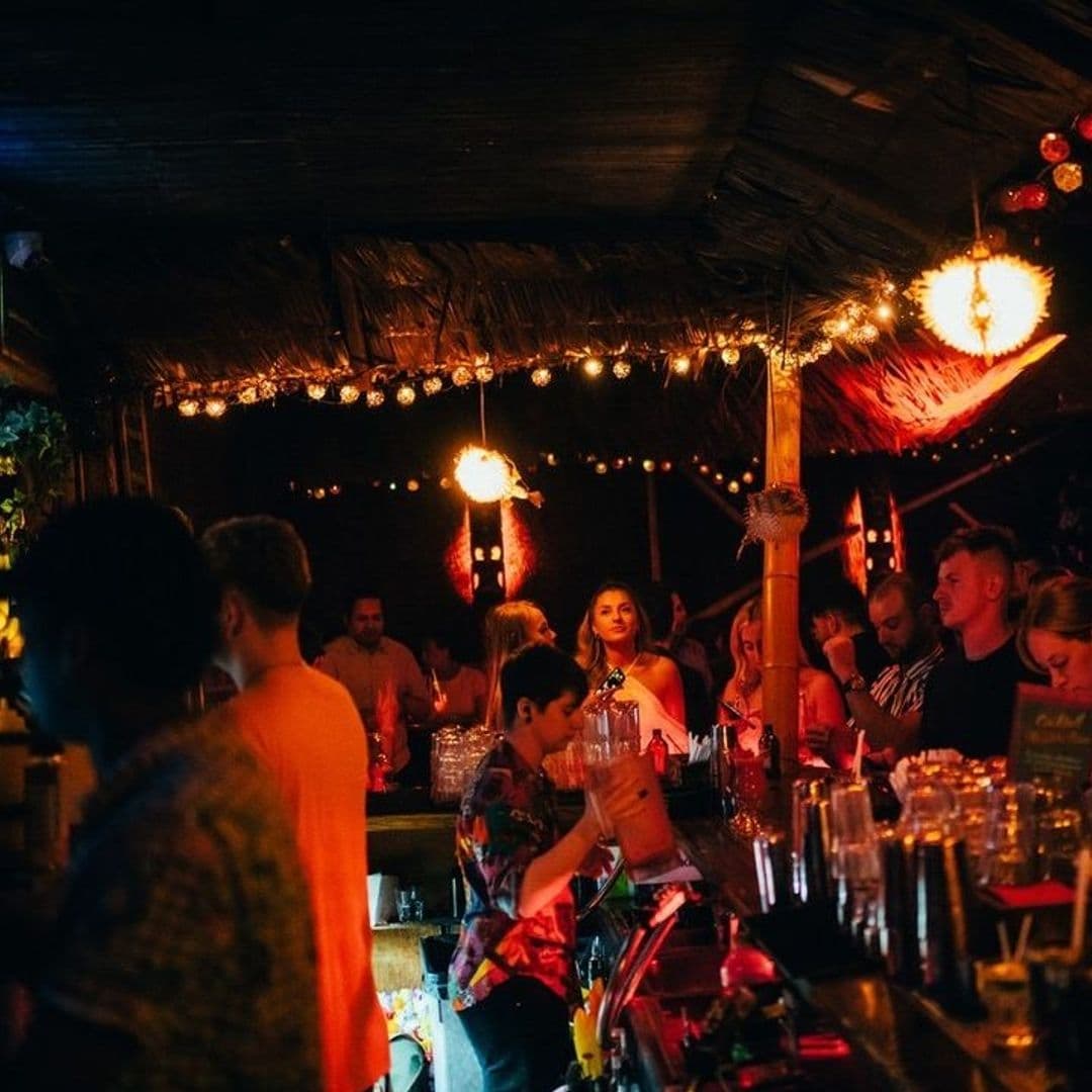 Vibrant nightlife scene at Tiki Hideaway with guests enjoying drinks and socializing under warm ambient lighting and tropical decor.