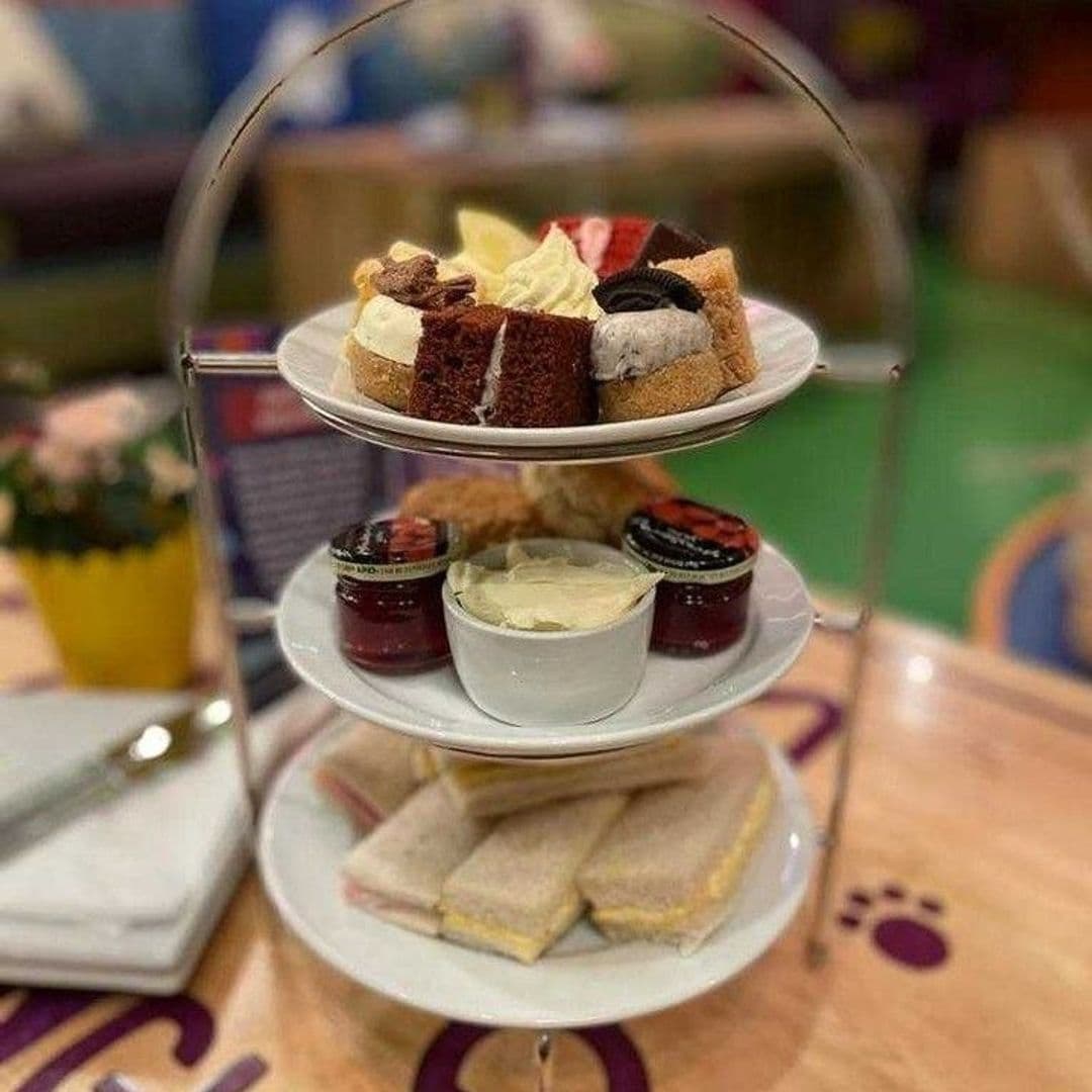 Three-tiered afternoon tea stand at Kitty Cafe, featuring an assortment of sandwiches on the bottom, scones with clotted cream and jam in the middle, and a selection of cakes and pastries on top.