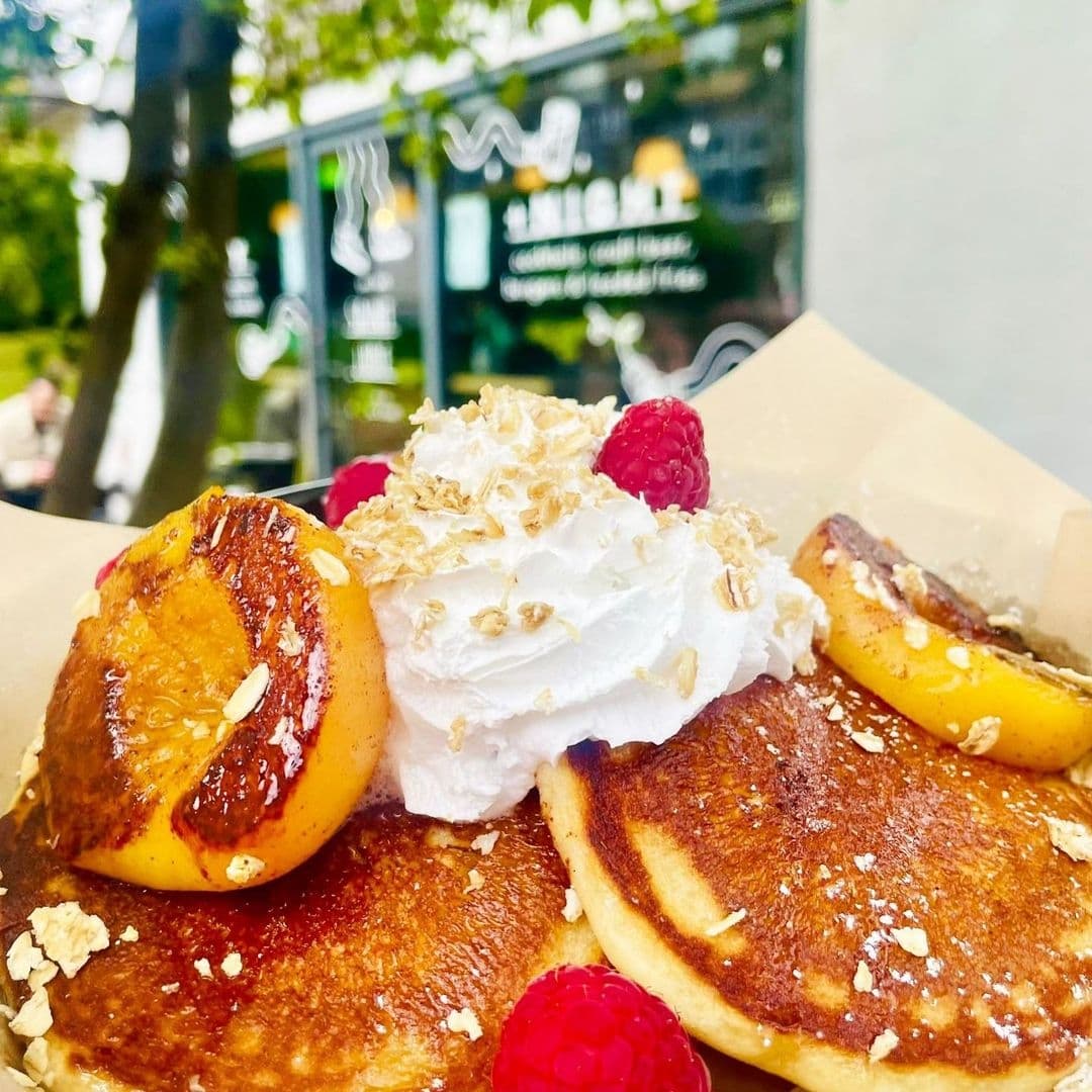 Delicious pancakes topped with whipped cream, fresh raspberries, and caramelized peaches at a café in Saint Jude.