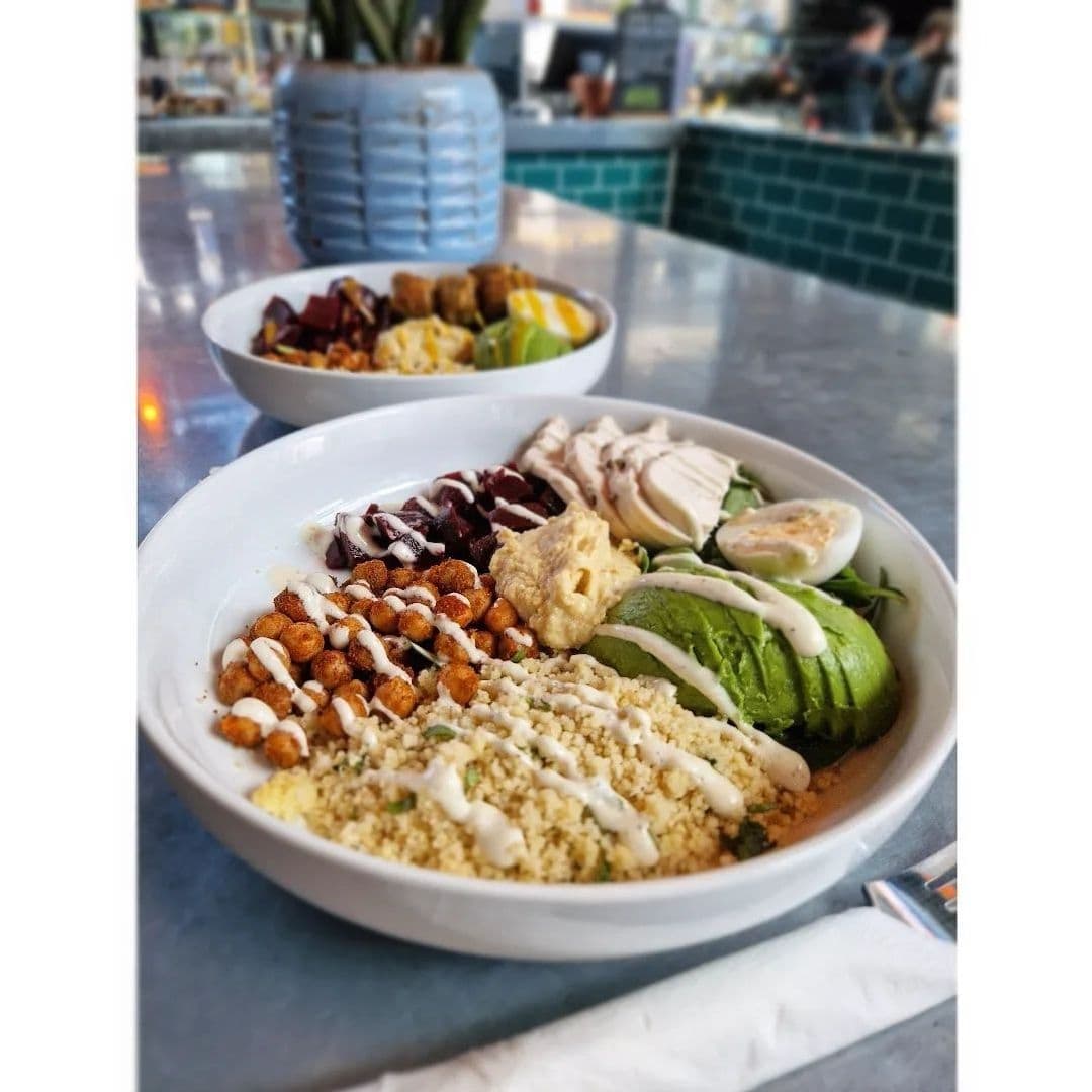 Fresh and healthy meal options at Sociable Folk with a close-up of a bowl containing couscous, chickpeas, avocado, hummus, and boiled egg, served in a casual dining setting.