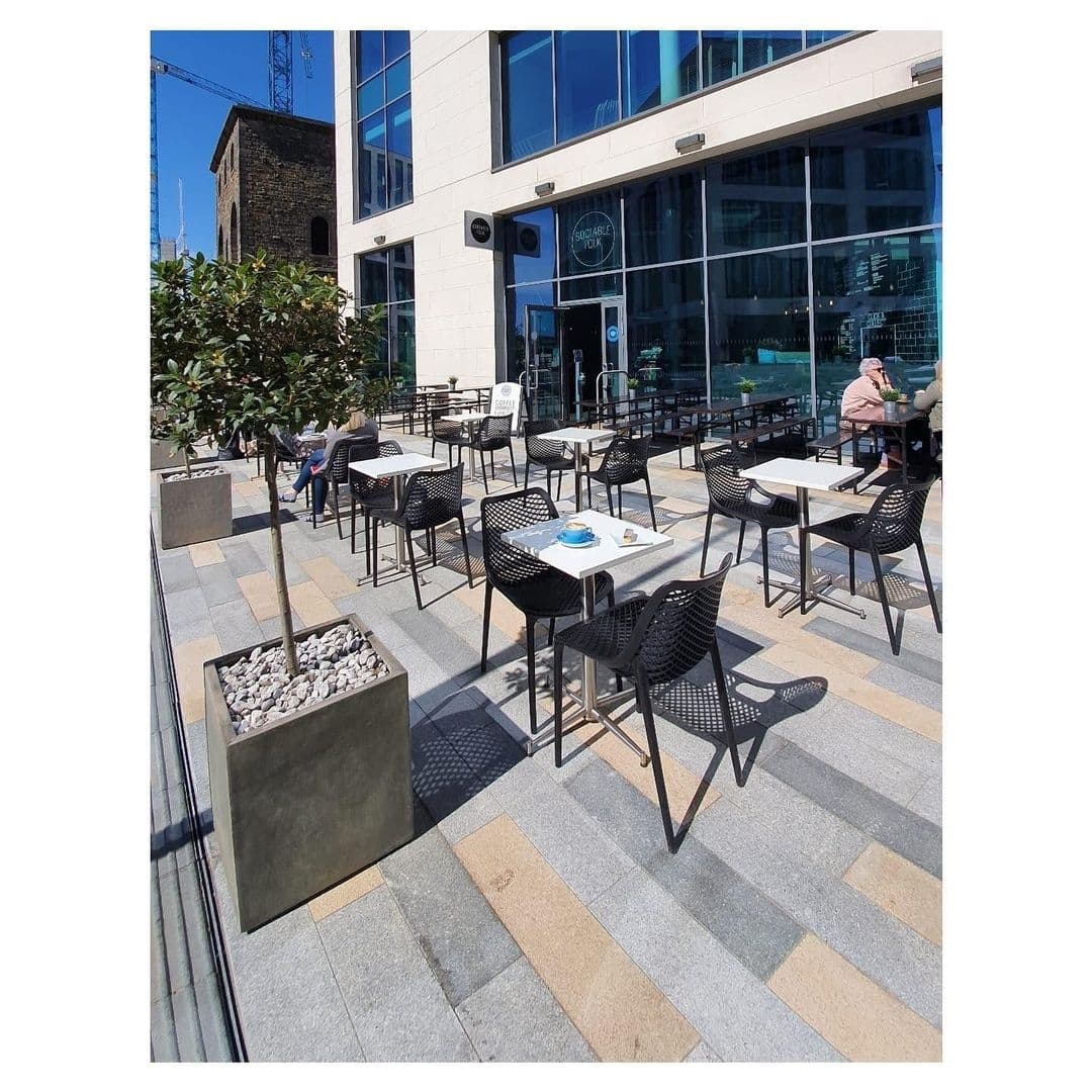Outdoor seating area at Sociable Folk with black chairs and tables on a sunny day, patrons enjoying the weather, and a clear view of the café's exterior.