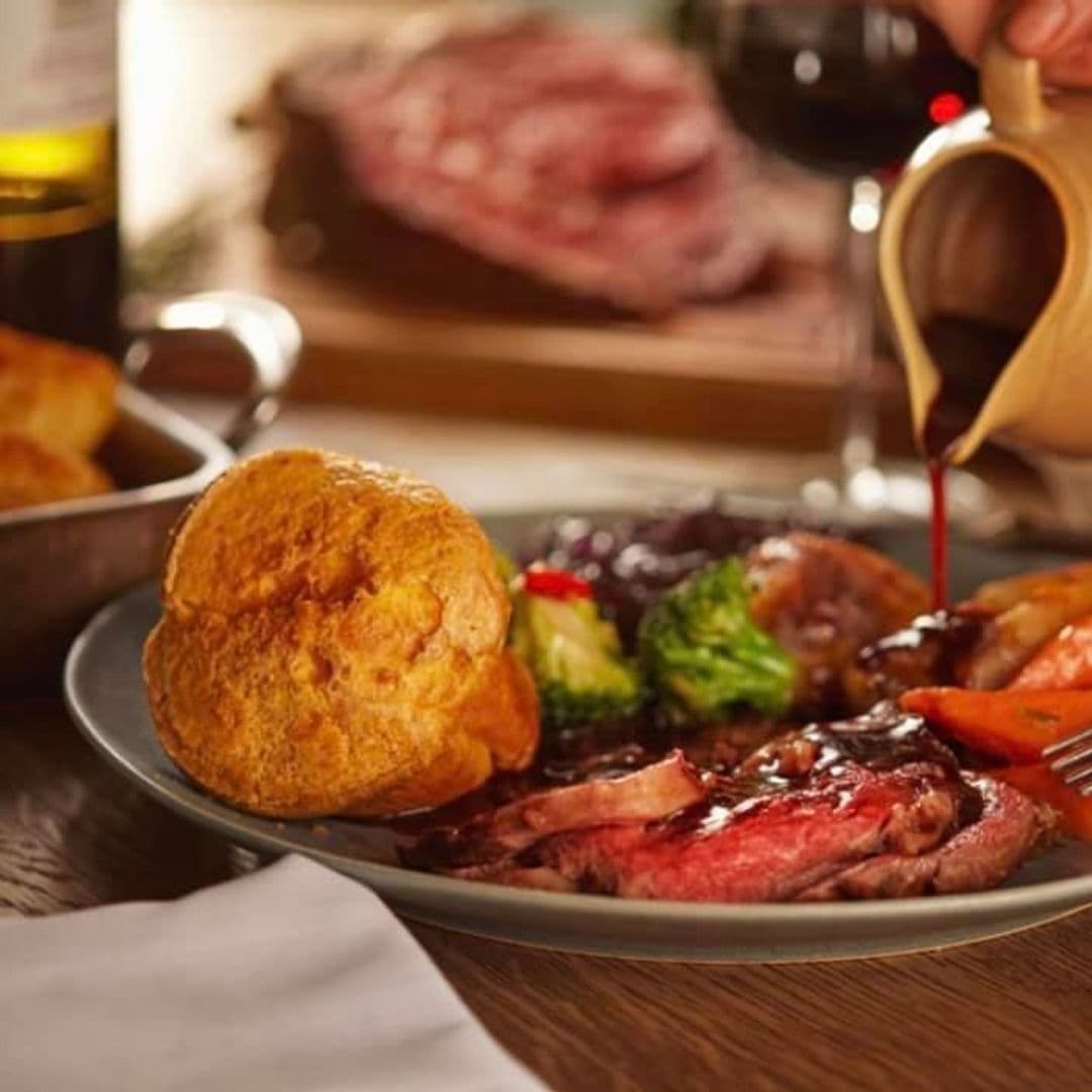 Traditional roast dinner at Bankhouse Inn with sliced beef, gravy being poured, Yorkshire pudding, and vegetables on a plate, accompanied by a glass of red wine in the background.