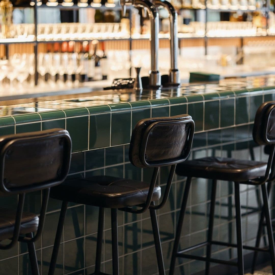 Elegant bar seating at Fearns Dock with green tiled counter and stylish black stools under modern lighting.
