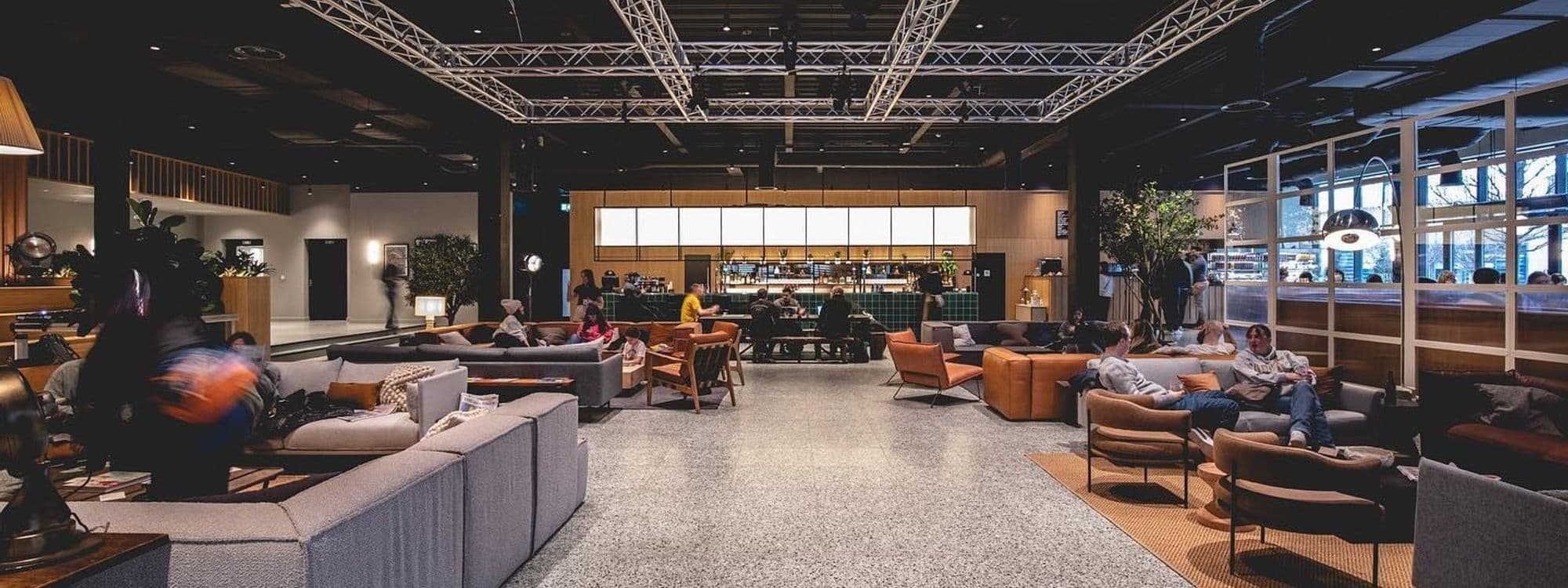 Interior view of Fearns Dock lounge area with visitors seated on sofas and armchairs, a bar counter in the background, and large windows letting in natural light.