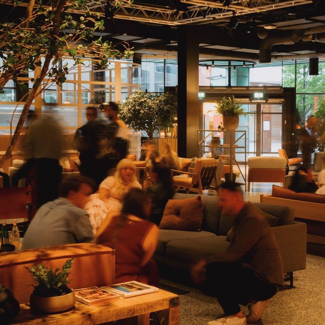 Alt text: "Vibrant social scene at Fearns Dock with people engaging in conversation on comfortable seating, surrounded by indoor greenery, with a warm and inviting ambiance."