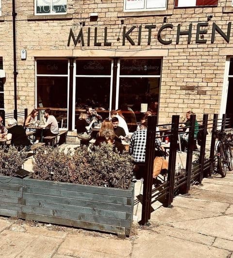 Outdoor seating at Mill Kitchen & Bakery with patrons enjoying meals under sunny skies, surrounded by greenery and parked bicycles.