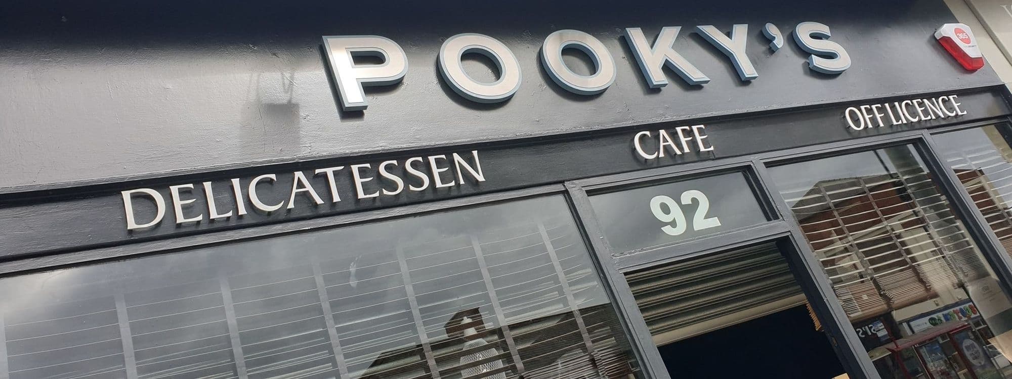 Exterior view of Pooky's Deli & Cafe, showcasing the signage with raised silver letters against a dark background, the address number 92, and a glimpse of the storefront windows.