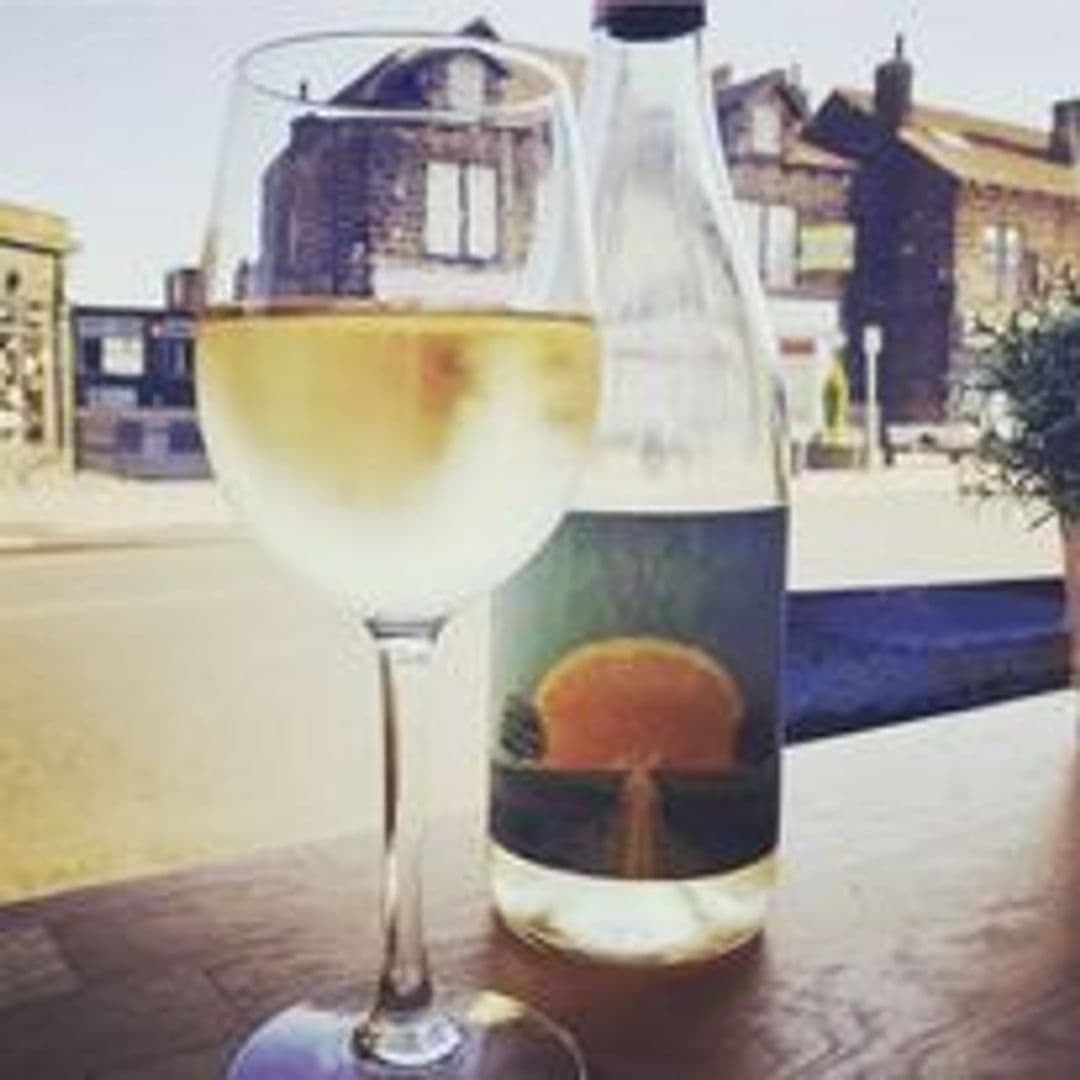 A chilled glass of white wine with a bottle on an outdoor table at Pooky's Deli & Cafe, with a blurred street view in the background.