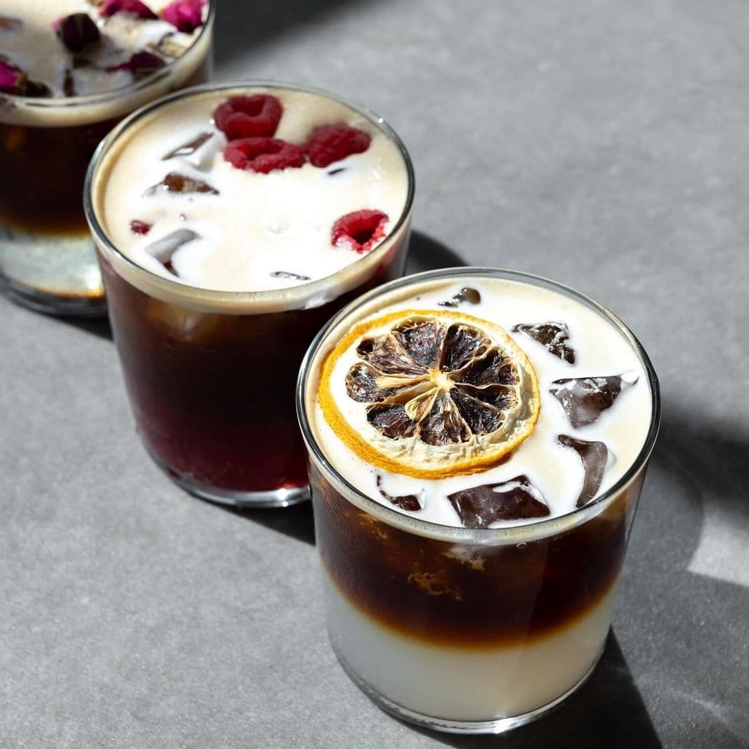 Alt text: "Three glasses of specialty iced coffee with artistic presentation at Raw Coffee, featuring one with a dried lemon garnish and another topped with fresh raspberries."