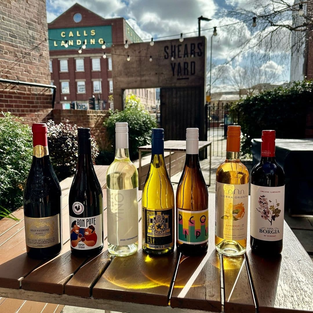 Selection of wine bottles on a wooden table at Shears Yard with the restaurant's sign in the background on a sunny day.