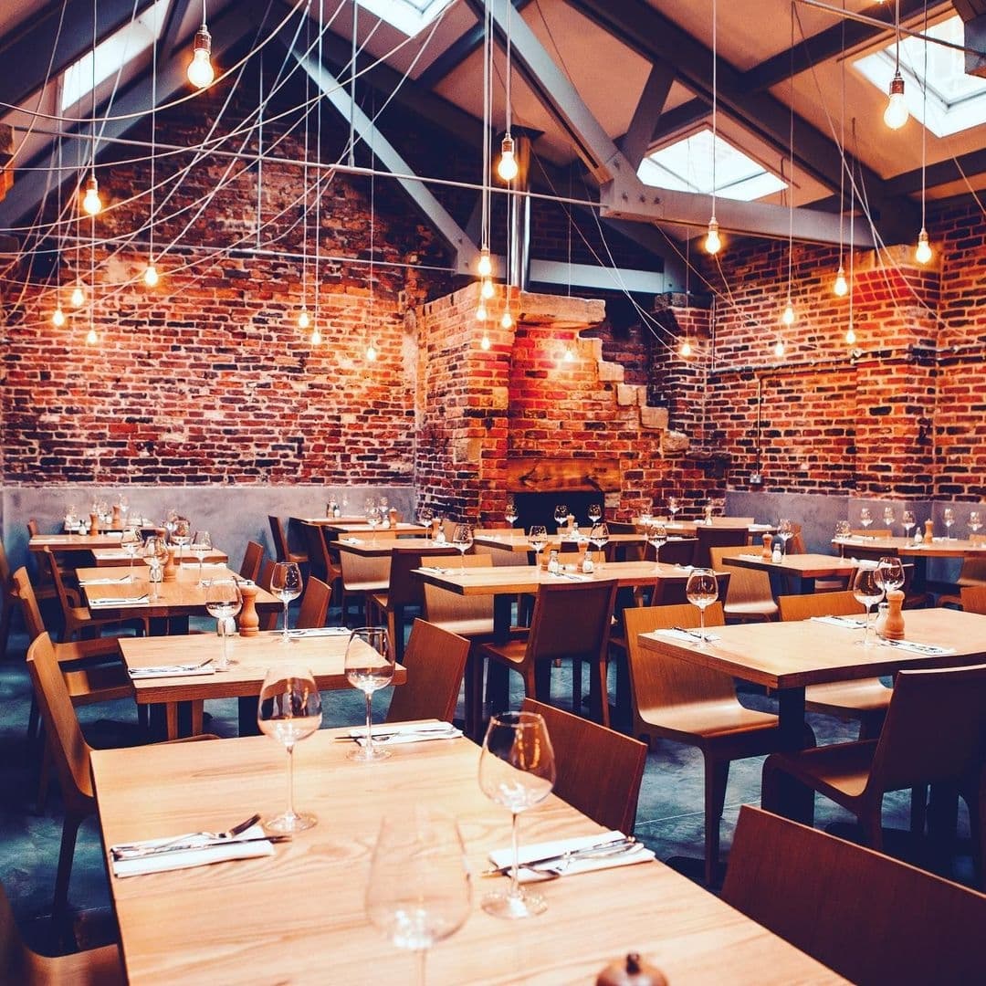 Interior of Shears Yard restaurant with exposed brick walls, hanging Edison bulbs, and wooden tables set for dining.