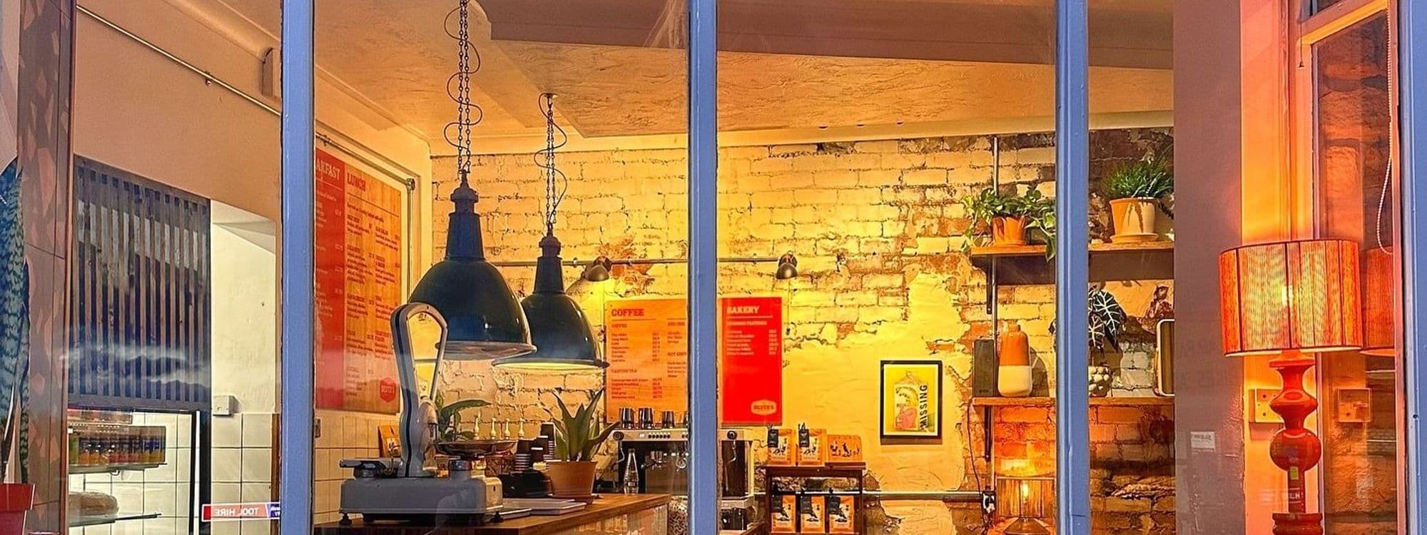 Interior of Silver’s Deli featuring warm lighting, vintage brick walls, hanging industrial lamps, and a cozy café setting with a visible menu board and potted plants.