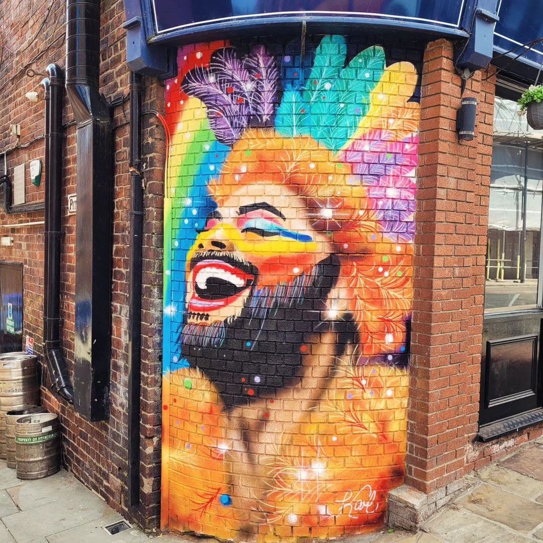 Colorful street art mural on the corner wall of The Bridge Bar, featuring a vibrant, laughing face with a rainbow of colors in the background.