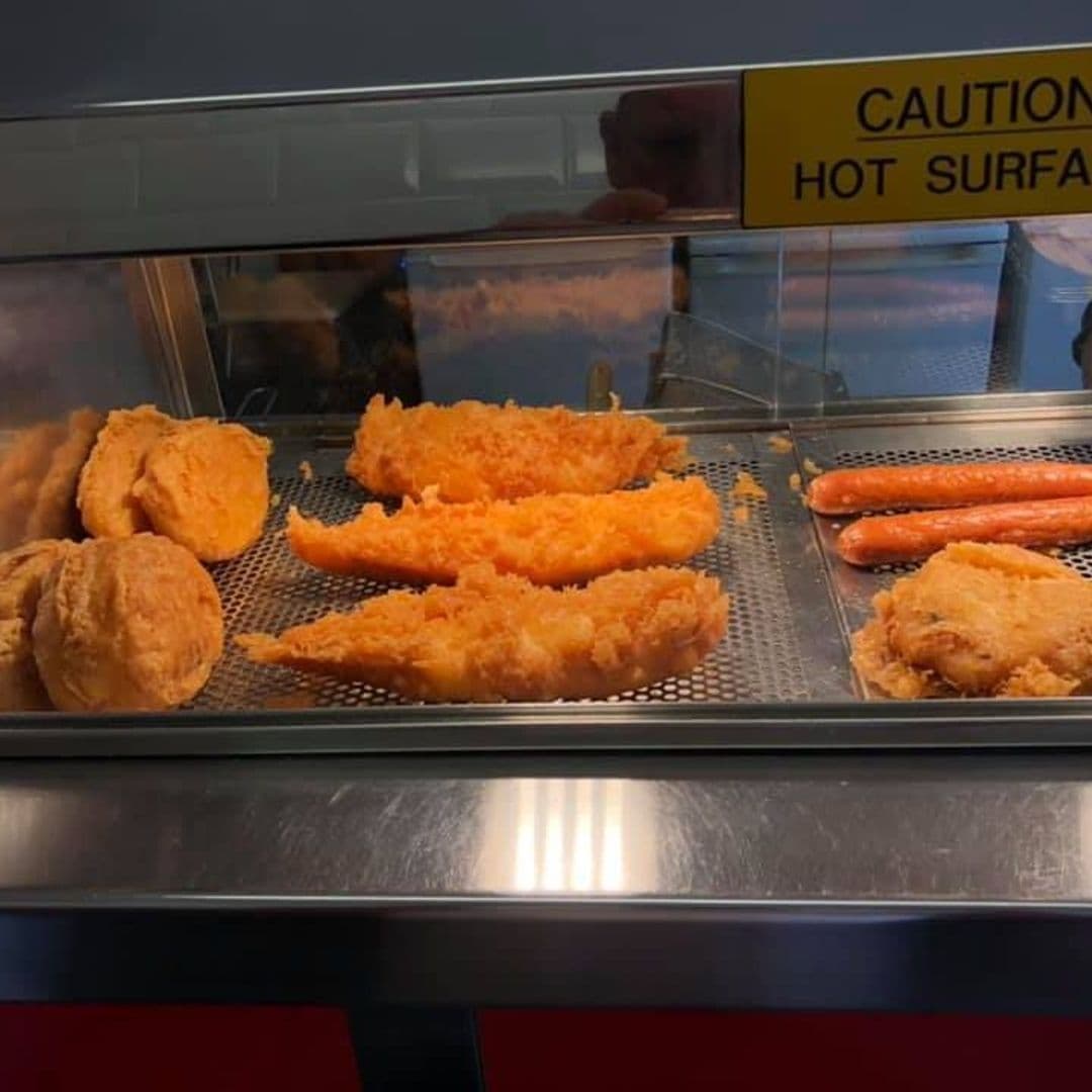 Assorted fried fish and sausages on display at The Deep – Pudsey, with a caution sign for a hot surface above.