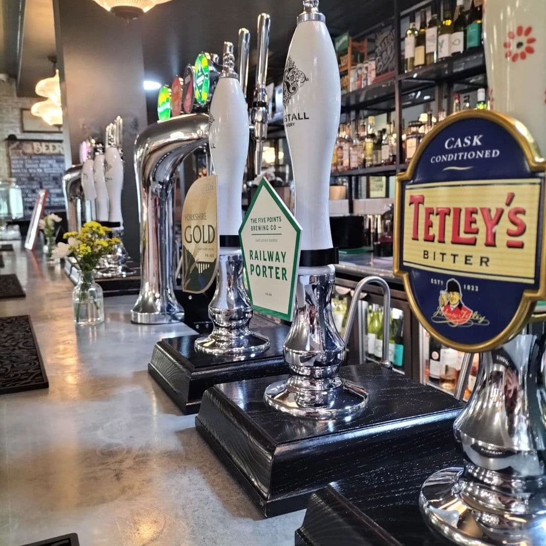 Close-up of beer taps at The Tetley bar, featuring a selection of beers including Tetley's Bitter, with a polished counter and blurred background.