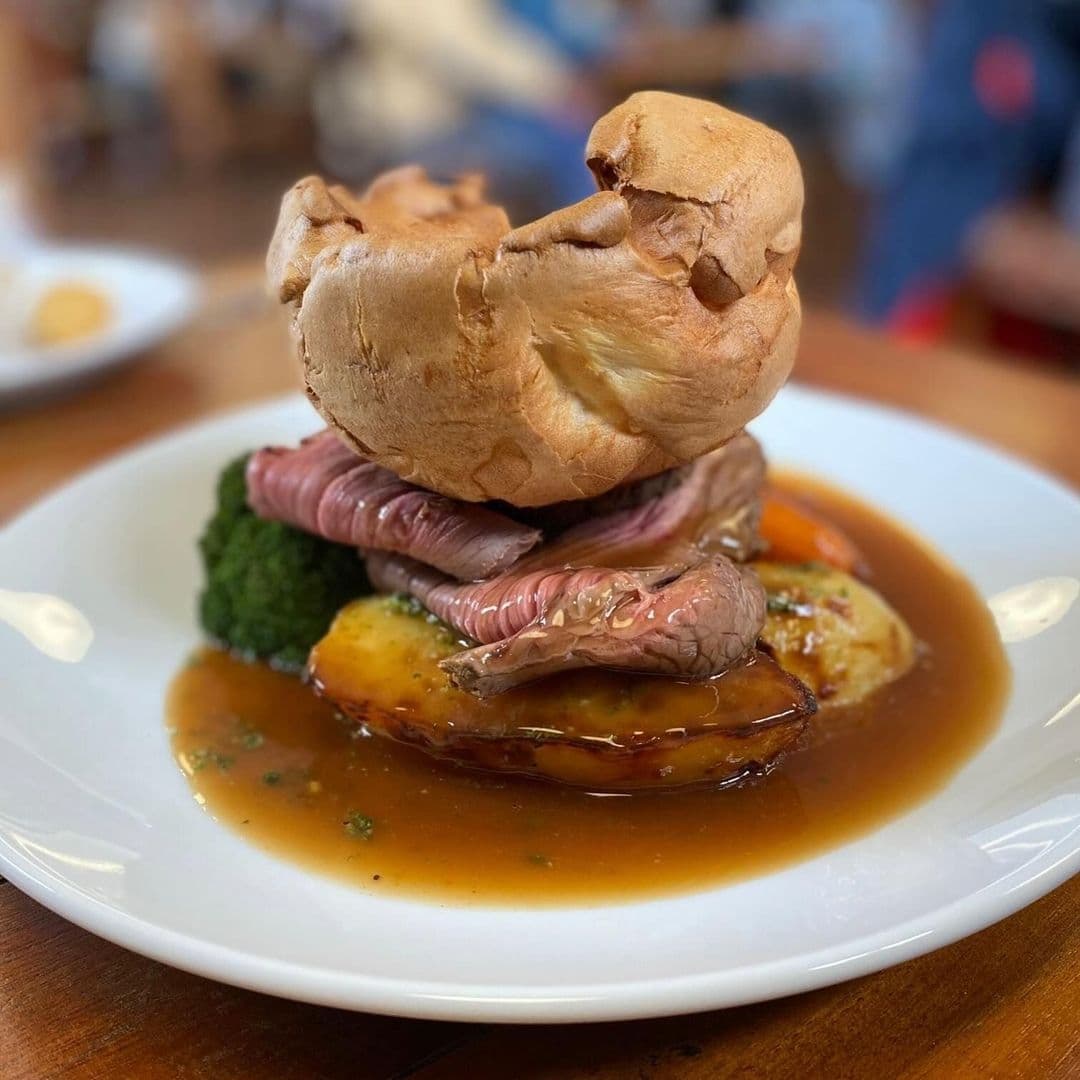 Traditional British Sunday roast with slices of roast beef, Yorkshire pudding, vegetables, and gravy served on a white plate at The Tetley.