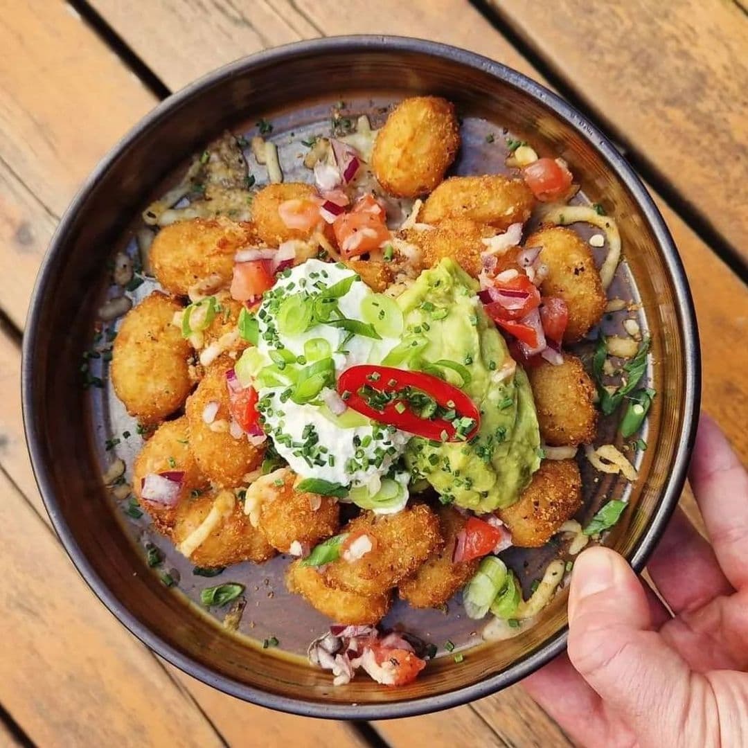 Appetizing bowl of golden-fried tater tots topped with fresh guacamole, sour cream, diced tomatoes, and sliced green onions, served at Treehouse Bar and Kitchen.