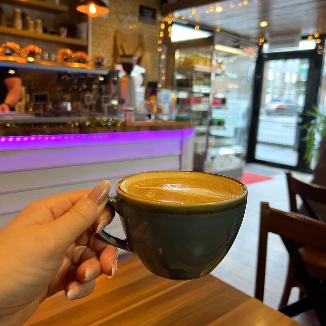 A hand holding a freshly brewed cup of coffee inside Unique Coffee&Bistro, with the cozy interior and coffee bar in the background.