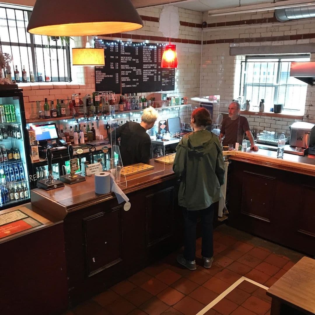 Interior of Wharf Chambers showing patrons at the bar with a selection of drinks on display, menu board in the background, and warm lighting.