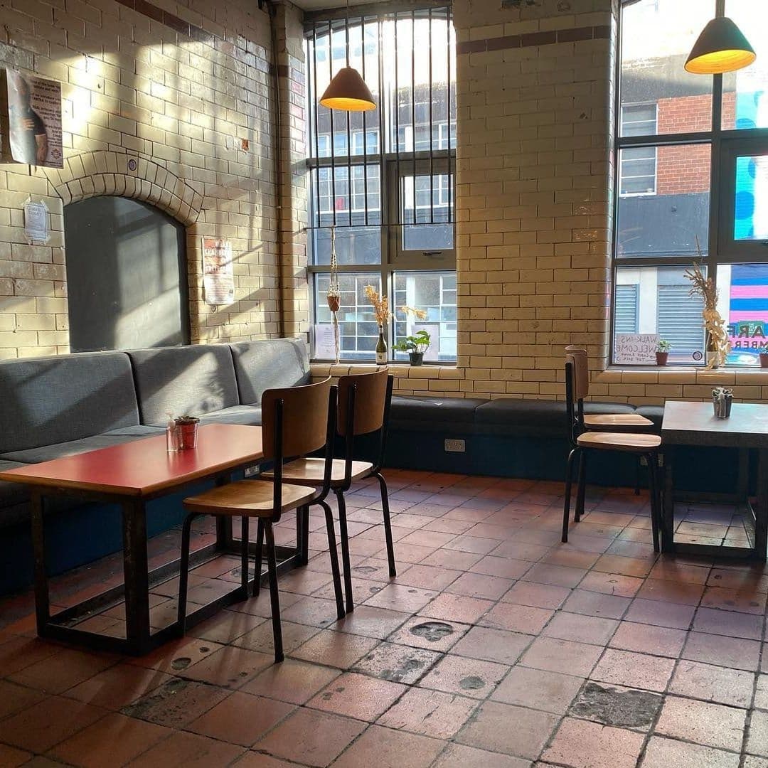 Cozy interior of Wharf Chambers with natural light streaming through large windows, highlighting the comfortable seating and warm brick walls.